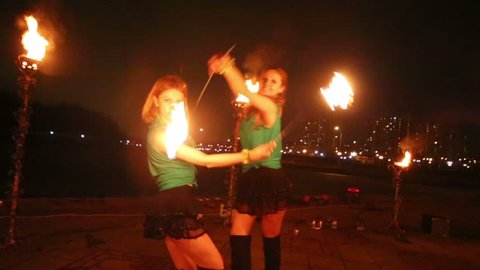 Two girls perform with burning torches at evening fire show.