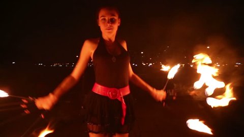 Young girl dances with burning torches made in shape of fans at fire show.
