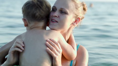 Little boy giving a hug and kissing mother while they bathing in sea on a sunny summer day