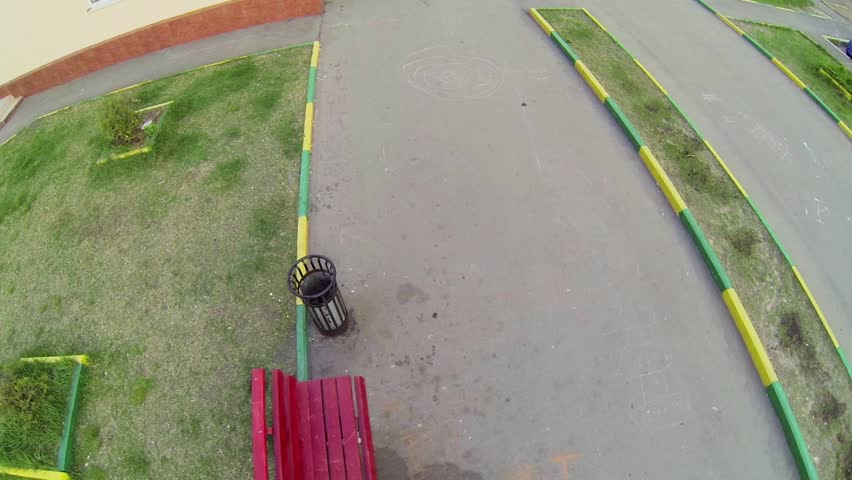 Little girl in helmet and kneepads passes on rollerblades by asphalt path. Aerial view