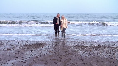 Slow Motion Shot Of Senior Couple Running Along Winter Beach