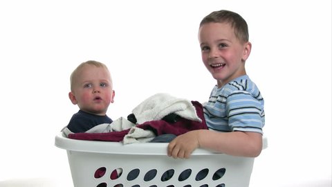 Two brothers playing together in a little laundry basket.  White background.