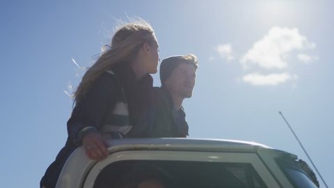 A couple stands in the bed of a pickup truck as it drives along a rural road.