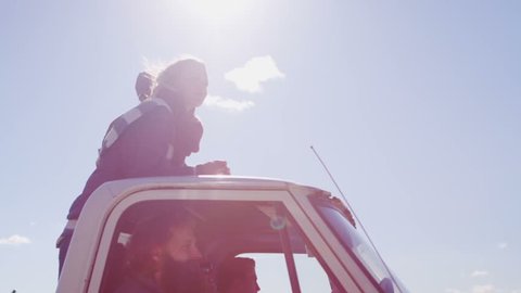 A couple stands in the bed of a pickup truck as it drives along a rural road.