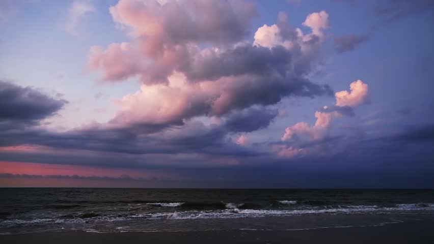 Ocean surf with billowing clouds above glowing pink in the light of the rising sun is featured in this looping footage shot at Emerald Isle, North Carolina. 