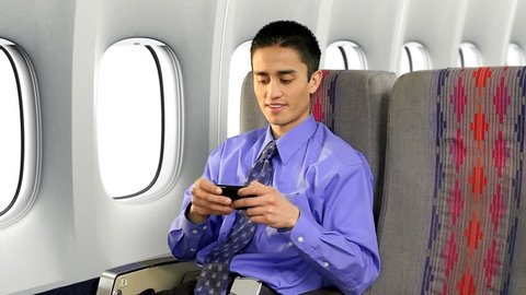 Businessman on commercial airplane using his cell phone to send a text message.