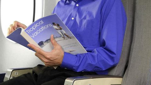 Passenger on a commercial airplane reading a travel magazine.