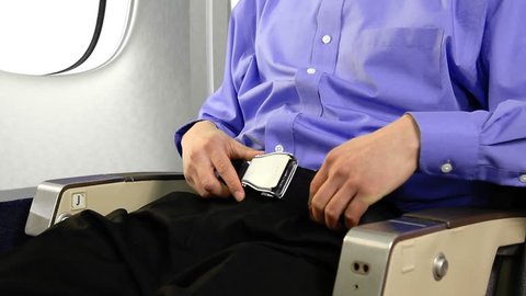 Passenger on a commercial airplane buckling and unbuckling his seat belt.