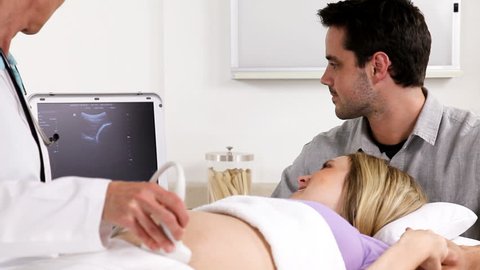 Doctor performing an ultrasound procedure on pregnant woman.