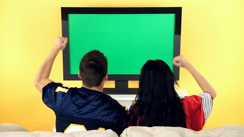 Two football fans watching the game on television. TV screen is chroma keyed for adding your own football video footage.
