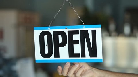 Business owner turning an open for business sign in their storefront window.
