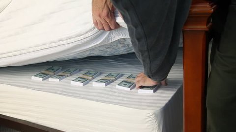 Man withdraws a stack of bills from the money he is hiding under his mattress.