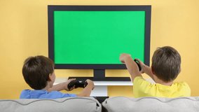 Two young boys playing video games at home on a flat screen television. TV screen is chroma keyed for adding your own video game screen.