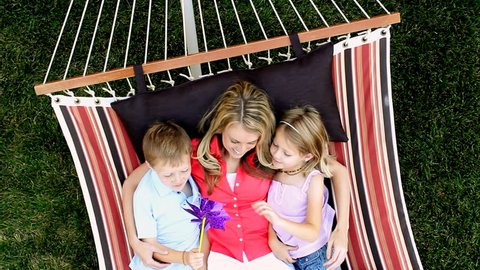 Mother and her two children relaxing outdoors in a hammock while playing with a pinwheel.