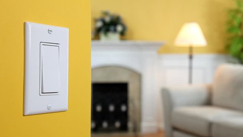 Wall light switch being turned off and back on again. View of a living room lamp is visible in the background.