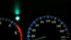 closeup of speedometer dashboard of car stopping beside the road due to heavy rain, turn left light is blinking with blurry view of moving traffic outside the road during raining