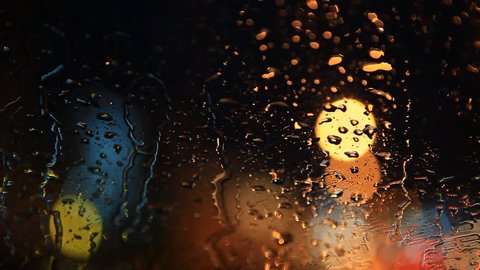 rain flows on the front windshield glass window of car stopping beside the road with beautiful colorful blurry light of traffic outside on the road, broken heart, sad, cry scene