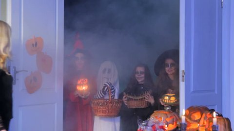 Children sing a trick-or-treat song and a woman gives them sweets.