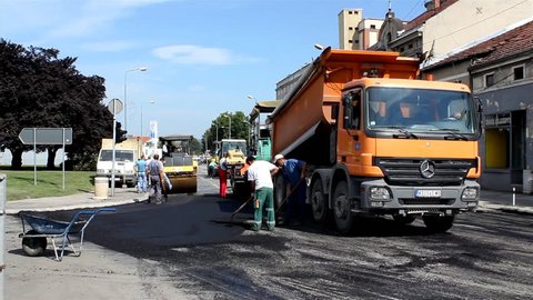 Srbija, Krusevac, 2014. Roadwork. Truck pouring asphalt in the machine for paving. Workers apply asphalt to road. Steamroller smoothing hot asphalt. Street repair, road construction. Roller. 25 fps.