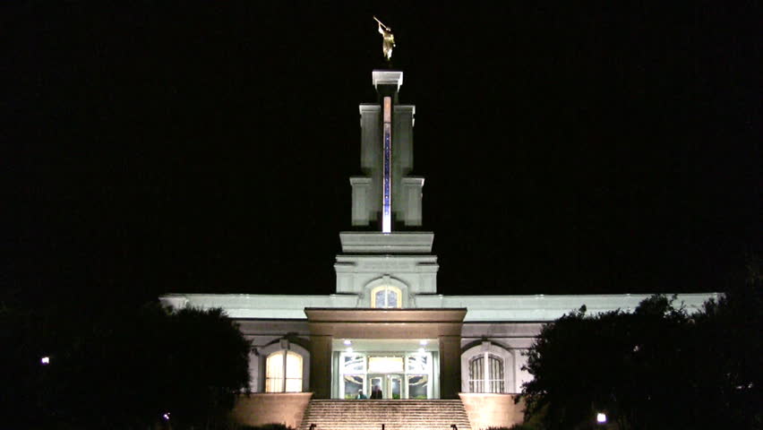 Video zoom in of a the Mormon or LDS Temple in San Antonio Texas at night. Bright lights with colorful accents. Waterfall garden in front with golden angel Moroni statue on top of steeple. 