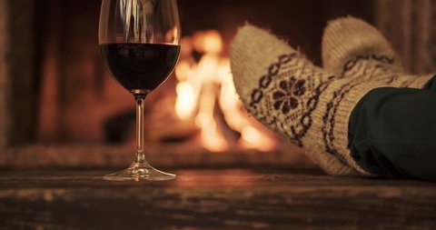Woman by the fireplace. Woman in woollen socks taking a glass of red wine relaxing by the cozy fireplace. Snug winter evening. Dolly shot. 4k graded from RAW.  วิดีโอสต็อก