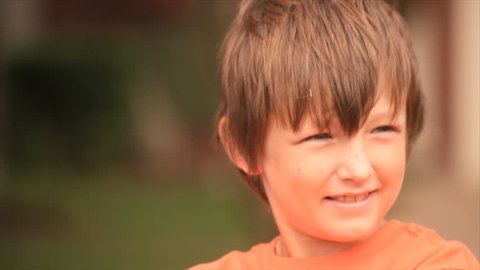 A portrait shot of a young boy sitting outside who looks at the camera and smiles.