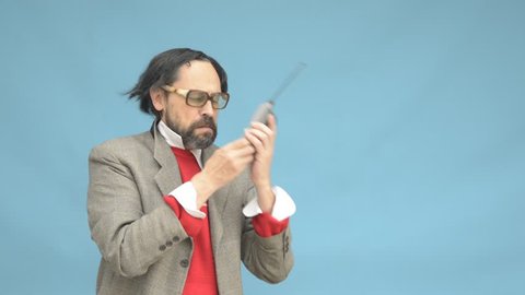An untidy bizarre man, wearing big patched glasses and a toupee, trying to answer an incoming phone call on an antique big cellphone, over light blue background