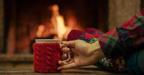 Woman relaxes by warm fire with a cup of hot drink and wriggles her toes in woollen socks.  Close up on feet. Winter concept. Slow motion 120 fps. Dolly shot. 4k graded from RAW. 