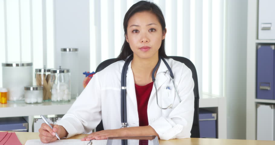 Asian doctor talking to camera at desk Royalty-Free Stock Footage #7445254