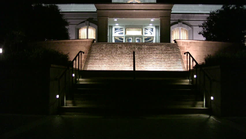 Video pan up then zoom in of the Mormon or LDS Temple in San Antonio Texas at night. Bright lights with colorful accents. Waterfall garden in front with golden angel Moroni statue on top of steeple.
