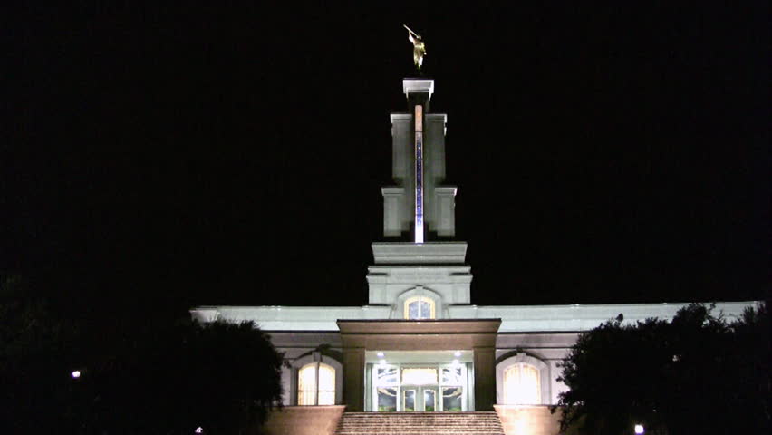 Video night of the Mormon or LDS Temple in San Antonio Texas at night. Bright lights with colorful accents. Waterfall garden in front with golden angel Moroni statue on top of steeple. 