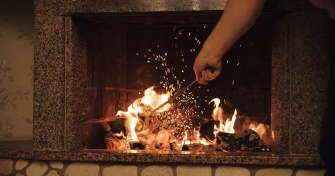 Adult man moving logs with a rake in a burning fireplace creating warm and cosy atmosphere. Slow motion 120 fps. 4k graded from RAW. วิดีโอสต็อก