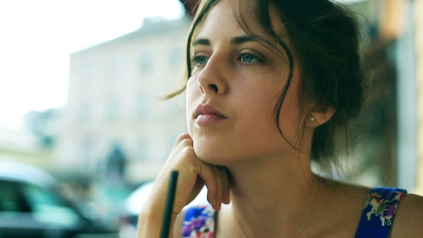 Sad girl sitting in the street cafe and playing with straw in cocktail
