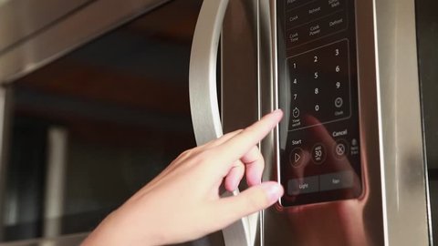 A woman using the timer on the kitchen microwave