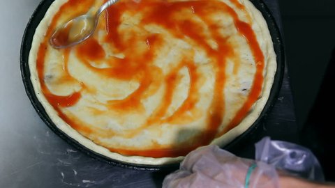 Pizzaiolo spreads dough with tomato sauce