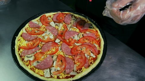 Pizzaiolo pouring salami on pizza