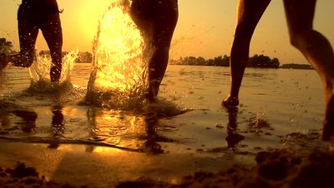 Group of happy girls running and playing in water at the beach on sunset. Beauty and joyful teenager friends having fun, dancing, spraying over summer sunset. Beach party. Sun flare. Slow motion 1080p