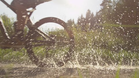 SLOW MOTION: Biker rides through puddle and splashes the camera