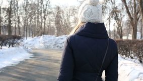 Young woman in white hat walks in park at winter day