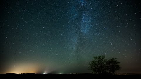 Night sky of stars time-lapse - Milky Way and glow above field and two trees
 库存视频