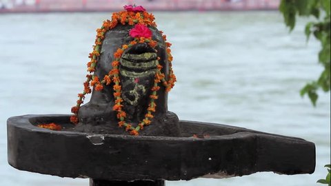 A close up shot of a Shiva-lingam, the generative symbol of the Hindu god Shiva with the Ganges River flowing in the background