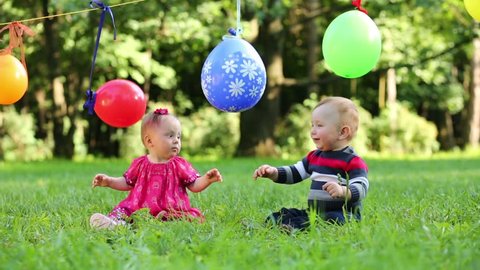 Colorful balloons hang on clothesline and two babies play with its at summer park