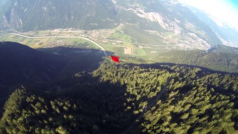 A base jumper in a wingsuit gliding down over a green landscape, POV