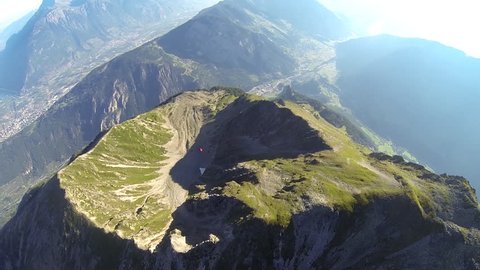 A base jumper in a wingsuit gliding down over a green mountain landscape, POV