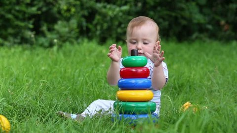 Happy baby plays with toys on fresh green grass of meadow