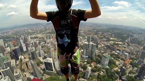 Two base jumpers jump together from a skyscraper, opens their parachutes in mid air before maneuvering it over the cityscape