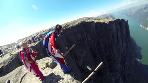 A base jumper jumps down from a cliff before gliding down in the air, a river visible below, POV