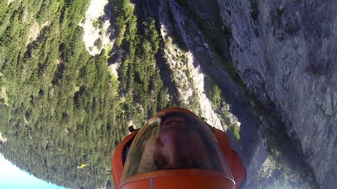 A base jumper in a wingsuit gliding down over a mountain landscape, POV