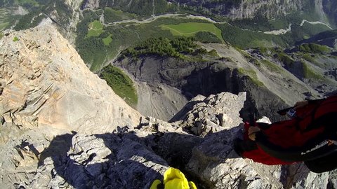 A base jumper in a wingsuit jumps from a rocky cliff, gliding down over a mountain landscape, POV