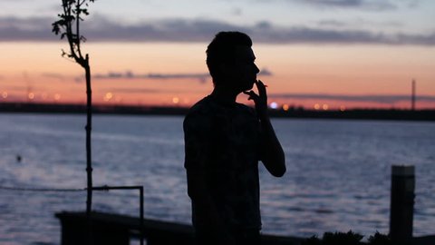 man smokes at the sunset near the river
